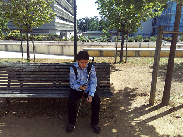 A blind person sitting on a park bench using its mobile device.