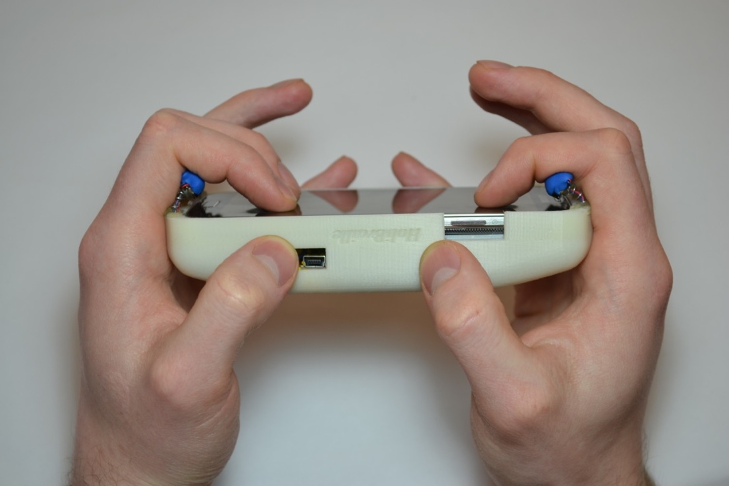 A case surrounding a mobile device and two hands holding the case with the device facing forward. Each hand has three fingers over a motor that provides haptic feedback.