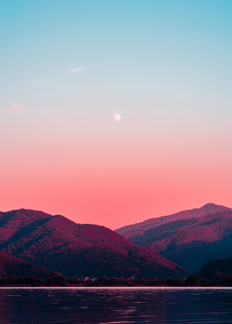 Landscape: moonrise over tree-covered mountains.