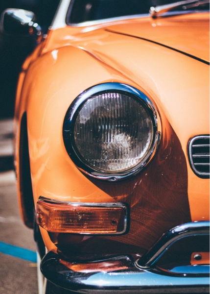 Viewing part of an orange car with an oversized headlight.