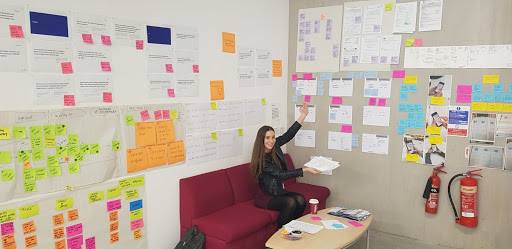 Photograph of team member pointing to the project wall, with post-its, service maps, insights and prototype testing stuck on there. 