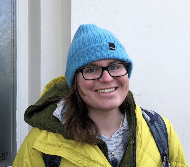 Kris Nóva smiling wearing a blue hat and hellow jacket