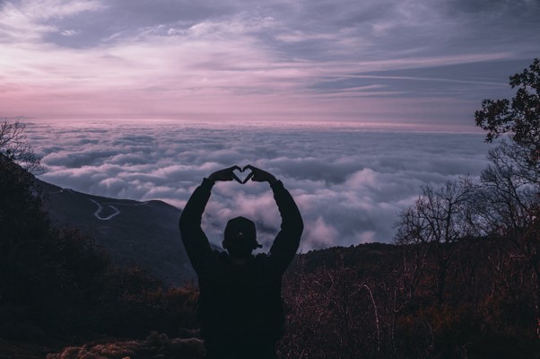 Person making heart with their hands in front of a purple sky