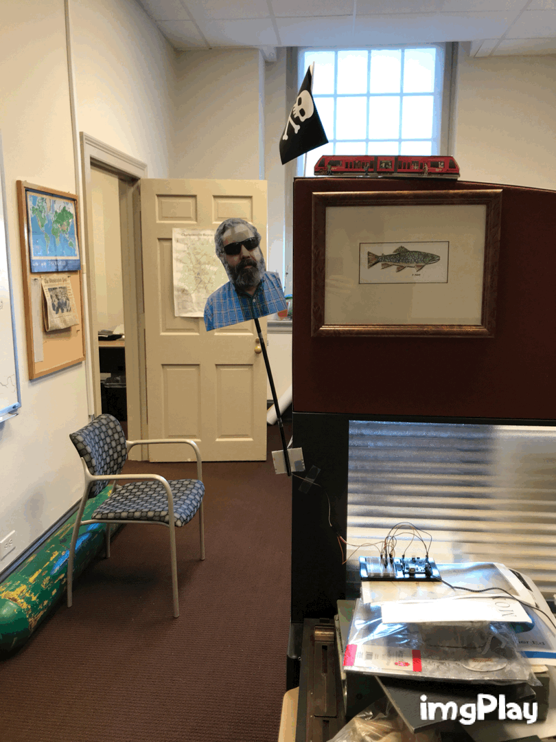 GIF of Drew MacQueen's "Arduino Chris", using electronics and a photo of GIS Specialist Chris Gist to turn the office lights back on when they go off from no one moving around.