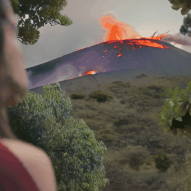 A_woman_looks_at_a_distant_erupting_volcano_captured_with_a_pull_back_cinematic_shot_4197508.gif