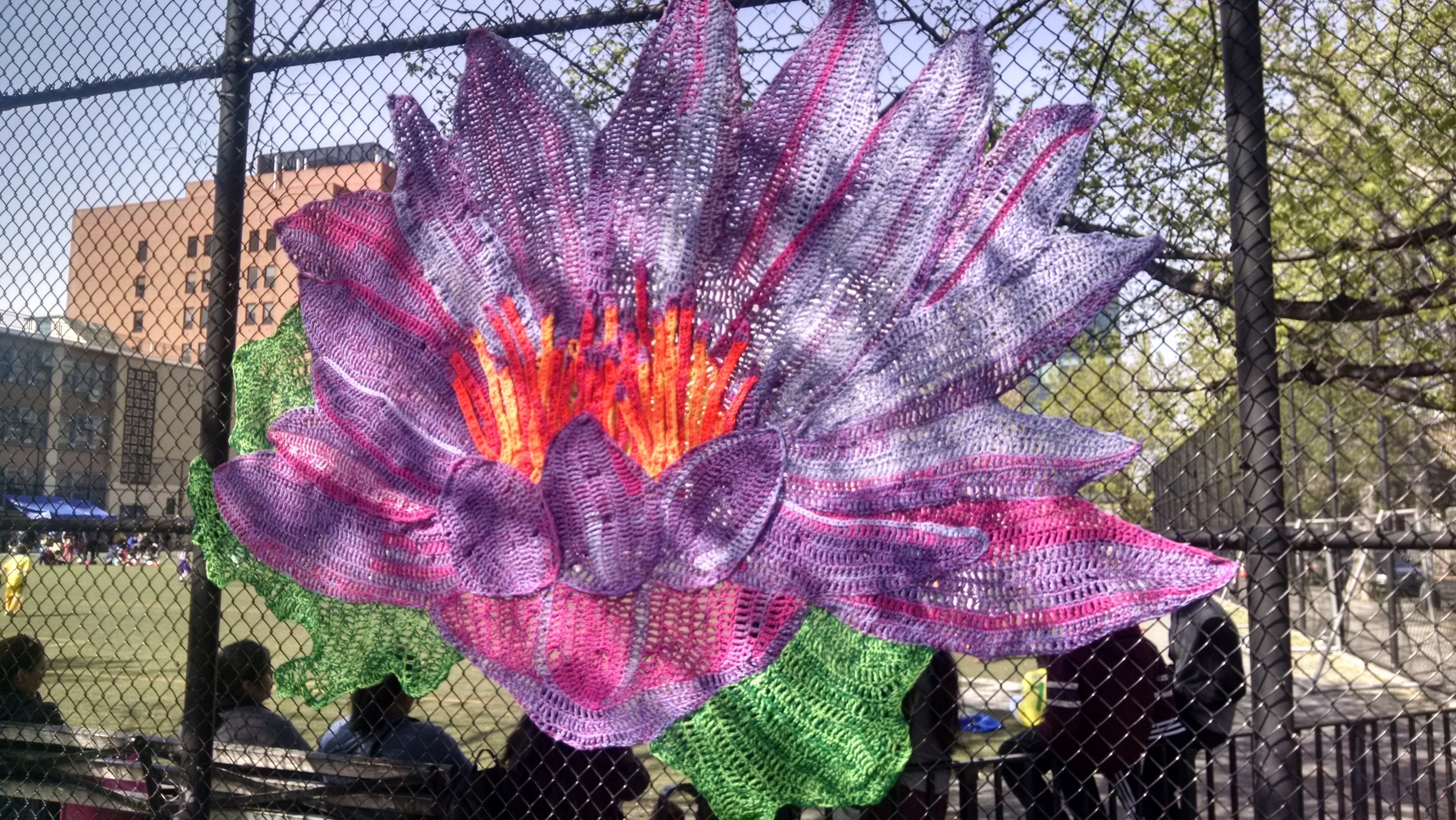 yarn weaved into chain link fence to make a large flower of pink and purple